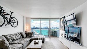 A modern living room with a grey sofa, a wooden coffee table, and a city view through large windows. - Best view in Miami Beach (Miami Beach)