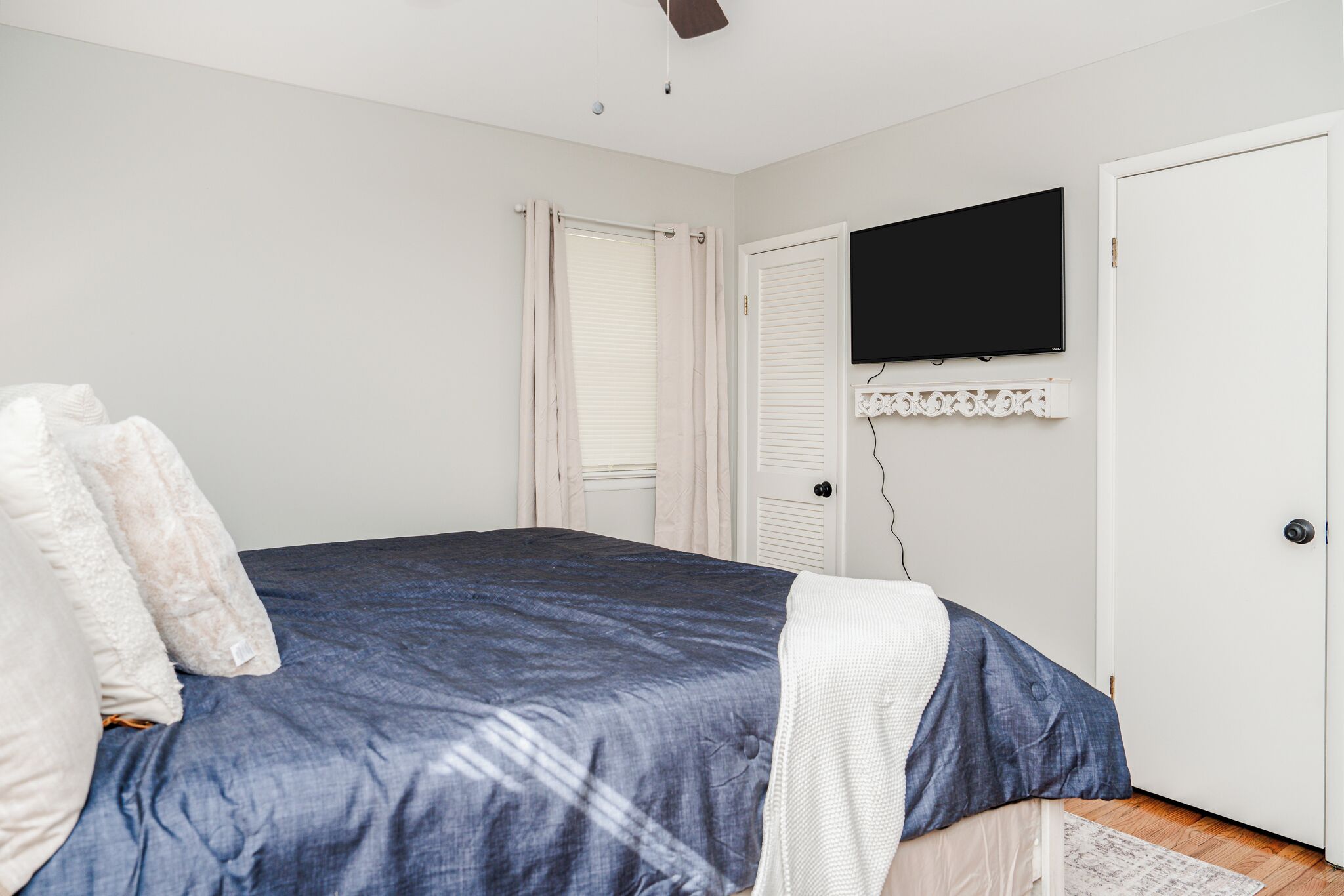 Une chambre à coucher avec un lit, un téléviseur à écran plat fixé au mur et une porte dotée d’un cadre blanc.