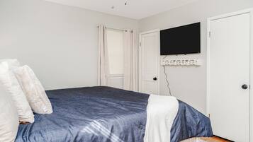 Une chambre à coucher avec un lit, un téléviseur à écran plat fixé au mur et une porte dotée d’un cadre blanc.