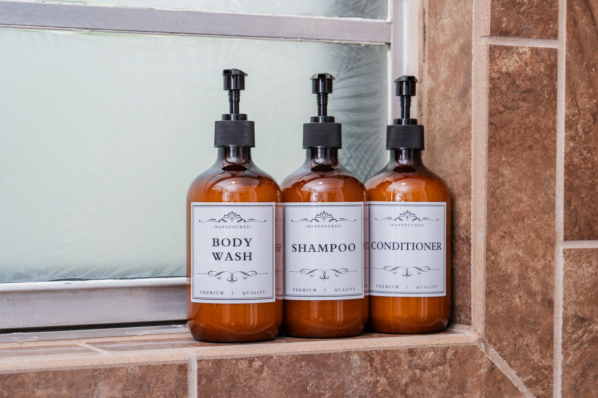 Trois bouteilles de gel douche, de shampoing et d’après-shampoing sont posées sur une étagère carrelée.