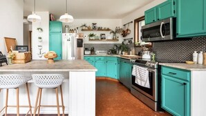 A kitchen with teal cabinets, a central island with stools, a microwave, and a stove. - Entire Cabin - Modern A-Frame w/Hot Tub (Ellenville)