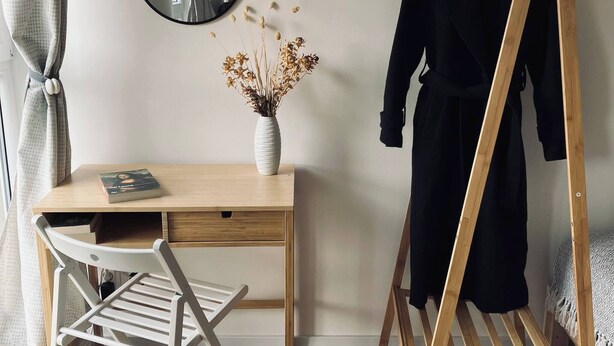 A room with a wooden desk, a mirror, a hanging clothes rack, a chair, and a vase with dried flowers. - Soul Apartment In The Center (Szczecin)