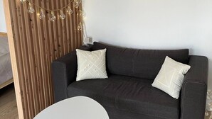 A modern living room with a dark grey sofa, two white pillows, a white round table with wooden legs, a wooden slat partition, and a macrame wall hanging. - Soul Apartment In The Center (Szczecin)