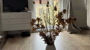 A living room with a white TV stand, a white table with a vase of dried flowers, and a window with curtains. - Soul Apartment In The Center (Szczecin)
