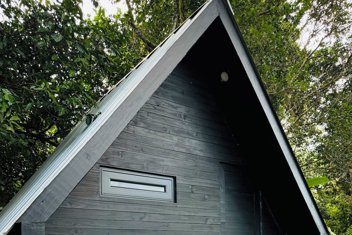 Una estructura moderna de madera oscura con techo inclinado, una pequeña terraza de madera y un ventanal.