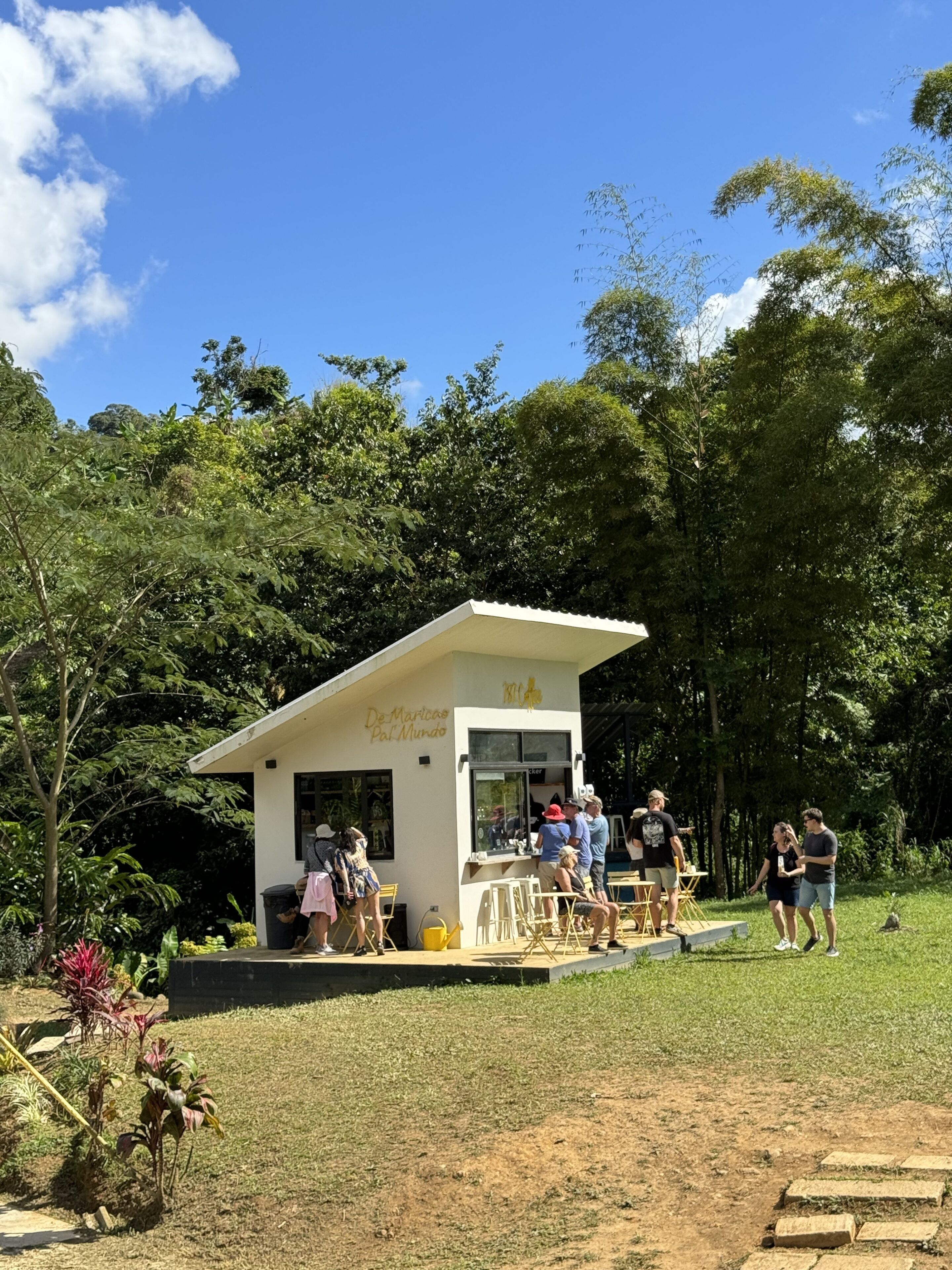 A small white kiosk with a sign reading "De Mariscos Pal Mundo" in a grassy area surrounded by trees.