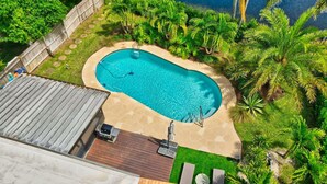 An aerial view of a backyard with a swimming pool, surrounded by lush greenery and a wooden deck.