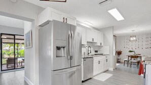 A modern kitchen with stainless steel appliances, white cabinetry, and a dining area with a table and chairs.