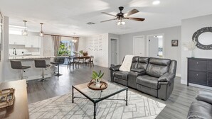 A modern living room with a leather sofa, a coffee table, and a dining area with bar stools.