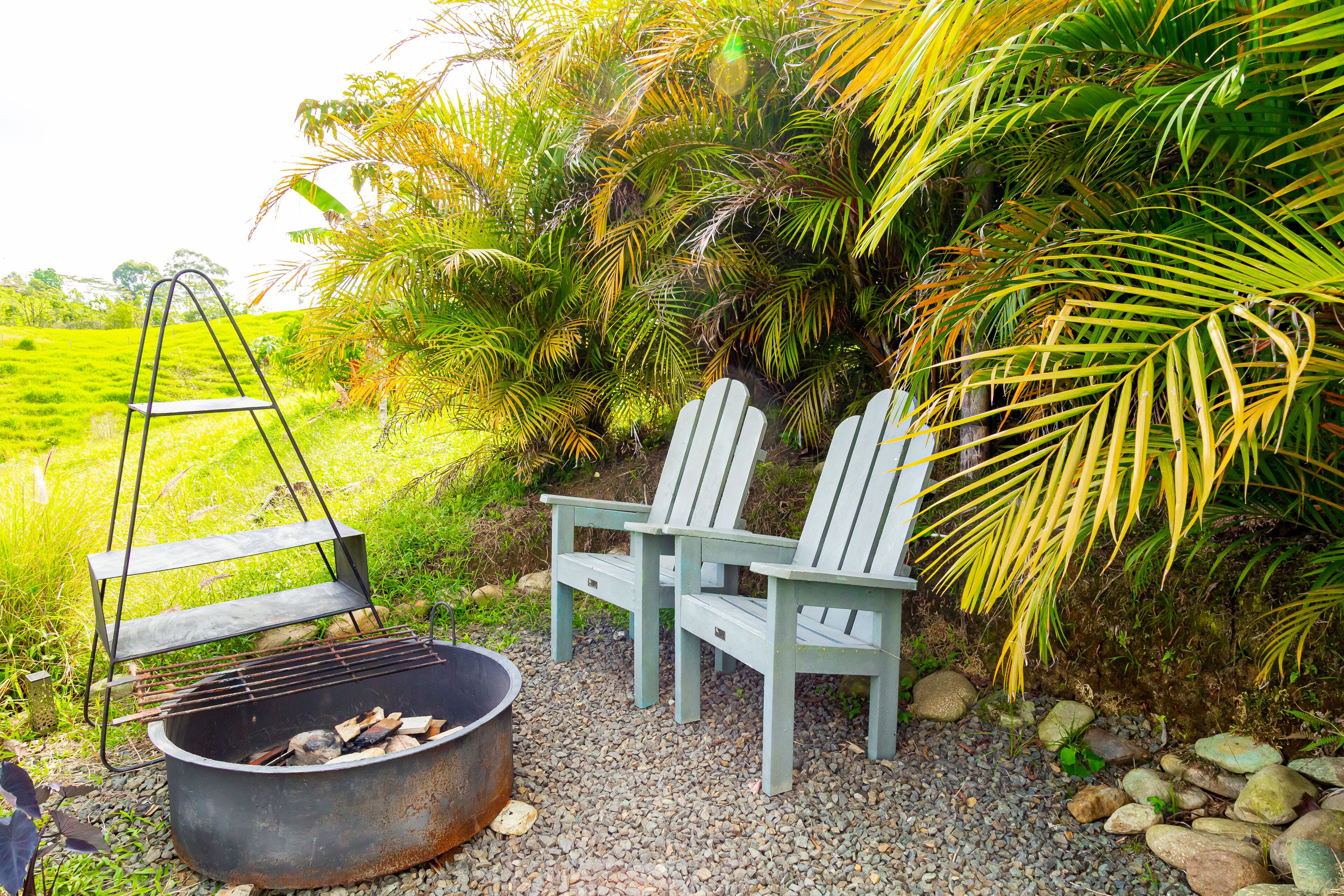 A rustic outdoor seating area with a metal grill and two Adirondack chairs.