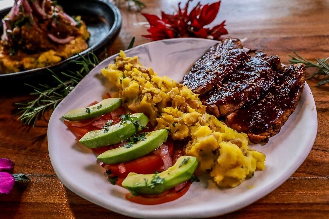 A plate with scrambled eggs, avocado slices, and a glazed meat dish.