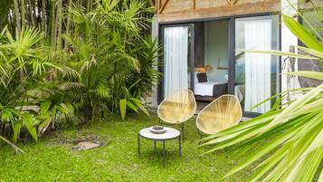 A lush garden with bamboo, a small round table with a bowl, and two wicker chairs.