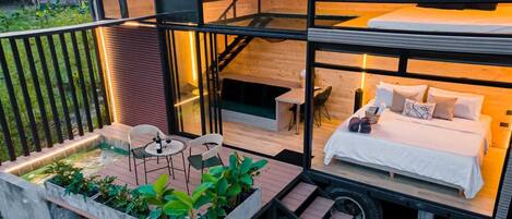Una habitación de hotel moderna y compacta, con cama, mesita de noche y un pequeño rincón de estar con sillas y una mesa.