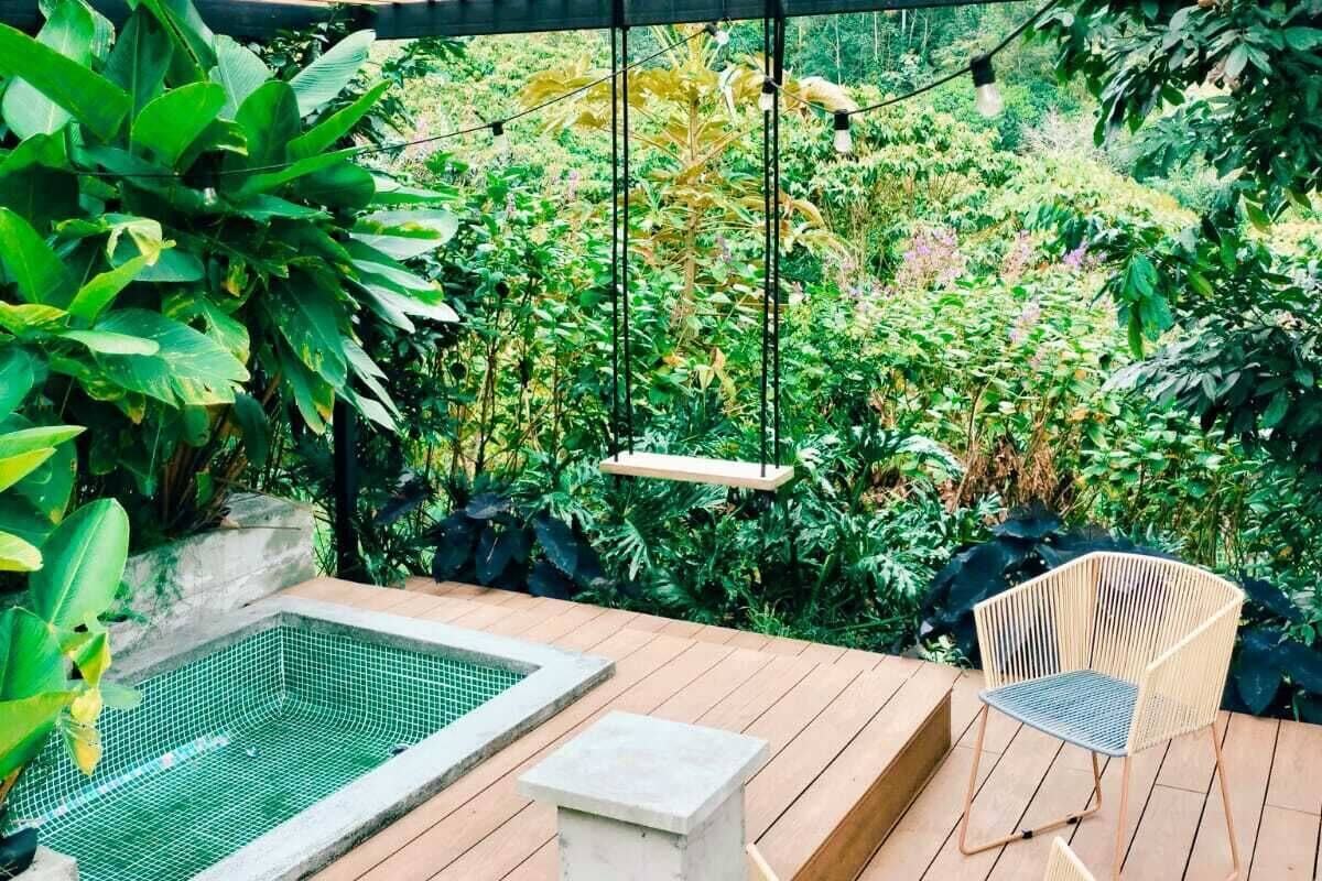 A wooden deck with a small pool, two wicker chairs, and a hanging light fixture.