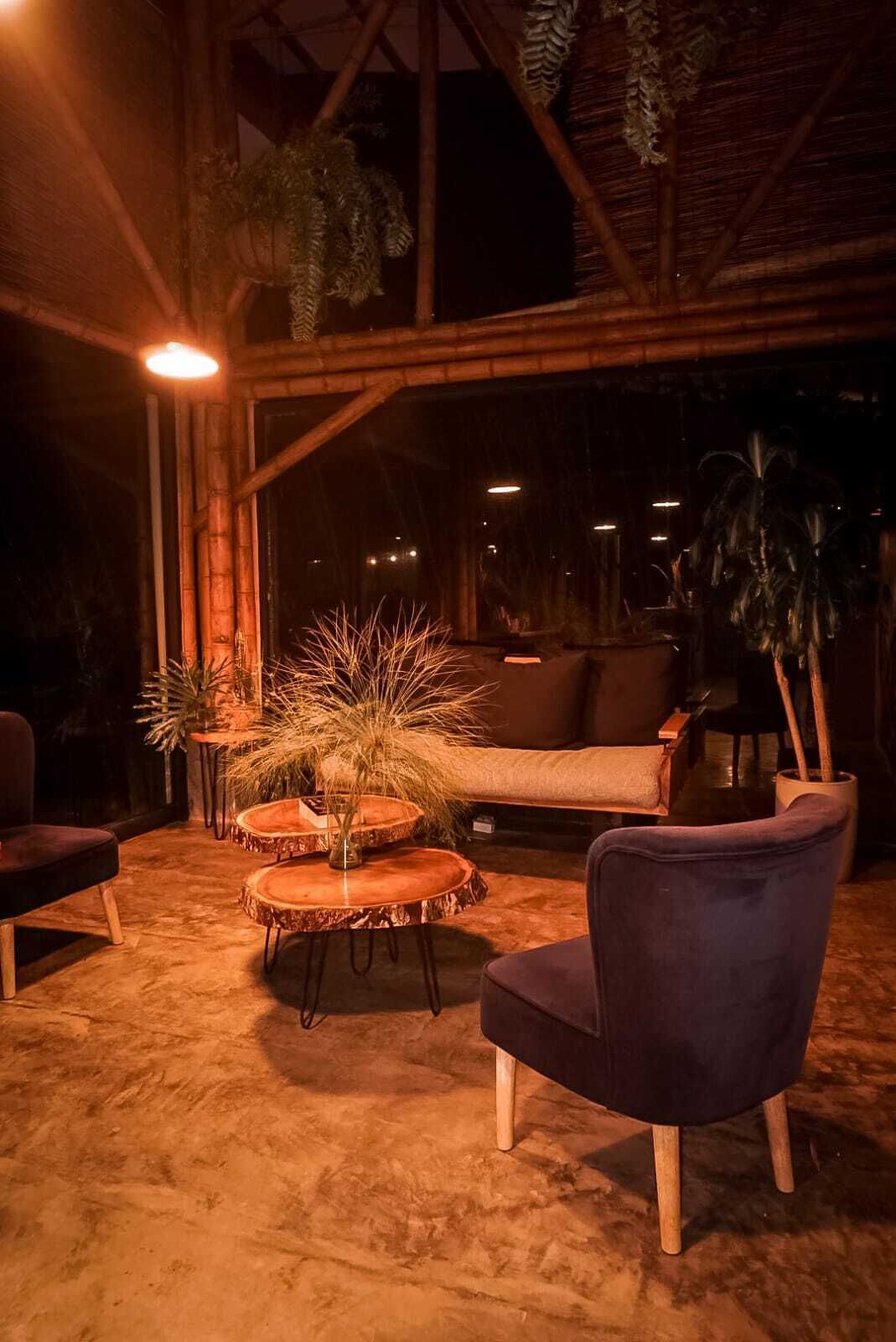 A cozy indoor seating area with round tables, a plush chair, and hanging plants.