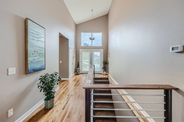 A hallway with a wooden floor, a staircase with metal railings, a potted plant, and a framed picture on the wall. - Lakewood Retreat Near Belmar (Lakewood)