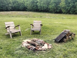 Deux fauteuils Adirondack en bois et un foyer avec des bûches, le tout installé dans un champ herbeux.