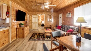 L’intérieur d’une cabane en bois comprend un coin repas, un canapé et un ventilateur de plafond.