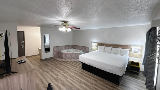 Une chambre d’hôtel comprenant un lit, un bureau, une télévision, un ventilateur de plafond, une salle de bain avec baignoire et une fenêtre avec des rideaux.