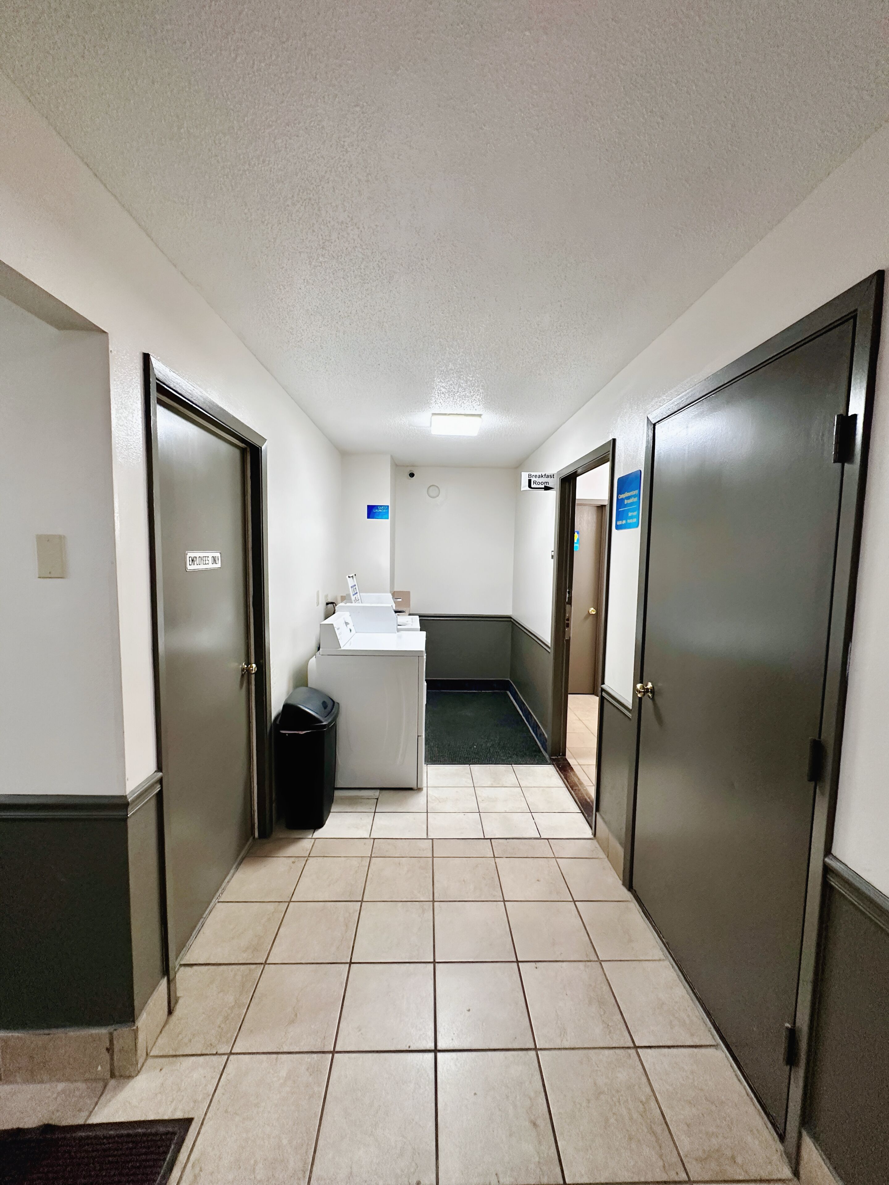 Un couloir avec des portes, une poubelle, un espace dédié à la buanderie et un panneau indiquant l’emplacement de la salle de petit-déjeuner.