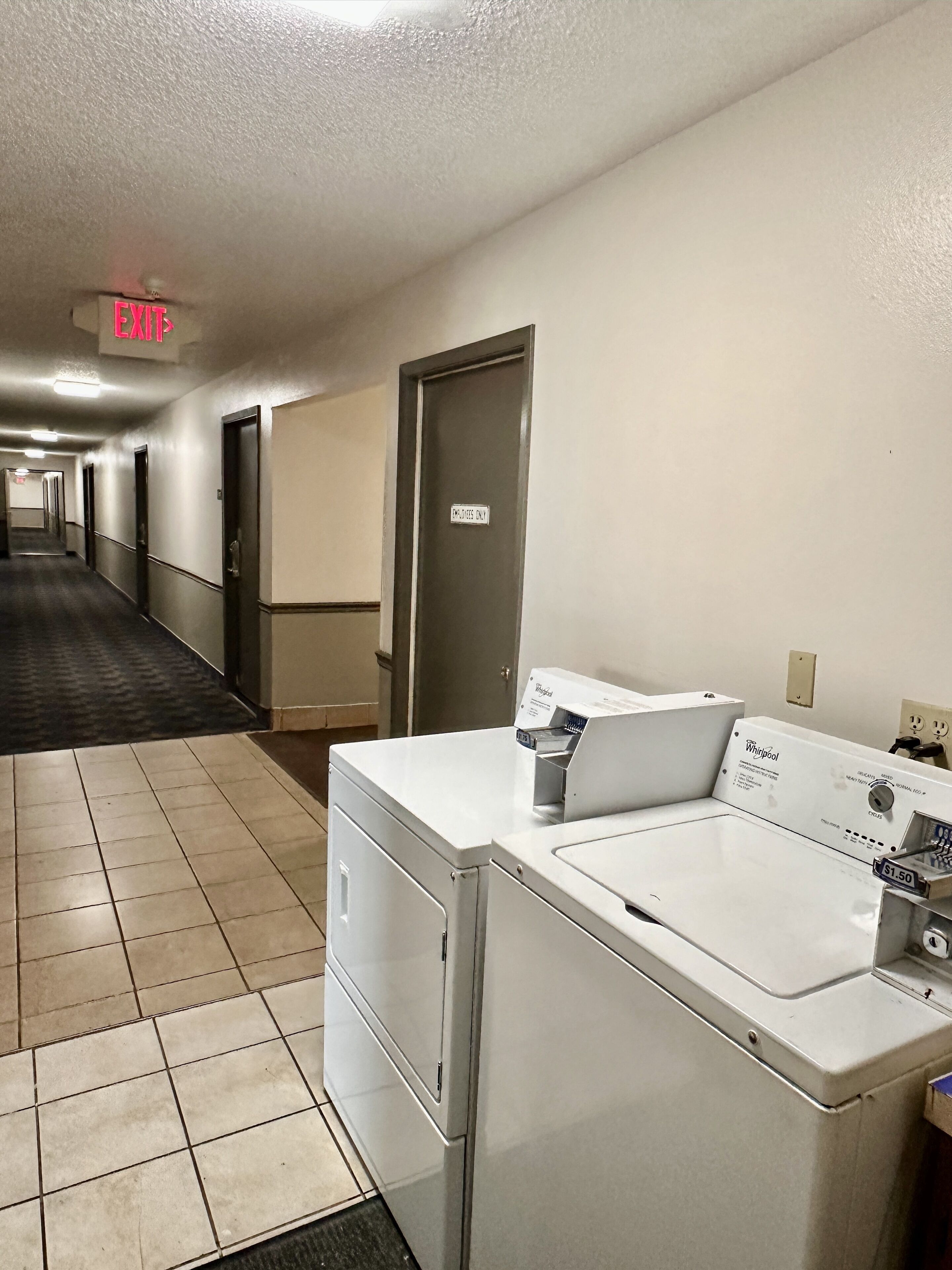 Un pasillo de hotel con un letrero de salida, una puerta que indica 'Solo personal' y una lavadora y secadora Whirlpool.