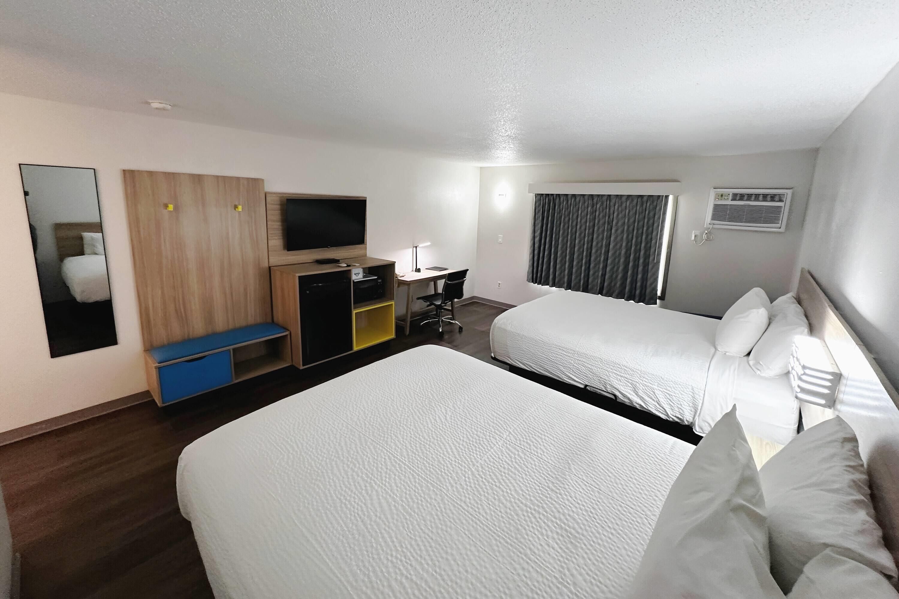 A hotel room with two beds, a desk with a chair, a TV, a wardrobe, and a mirror.