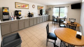 Une cuisine propre et bien éclairée, équipée d’une machine à café, d’une poubelle et d’un coin repas avec une table et des chaises.