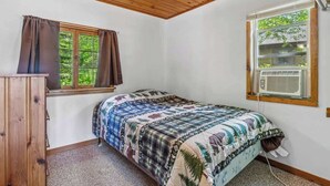 A bedroom with a bed, a window with curtains, a wooden ceiling, and an air conditioning unit. - Cabin #10 2BR 1BA Timberlane Resort (Park Rapids)