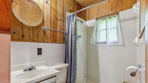 A bathroom with a wooden vanity, a toilet, a shower with a curtain, and a towel rack. - Cabin #10 2BR 1BA Timberlane Resort (Park Rapids)