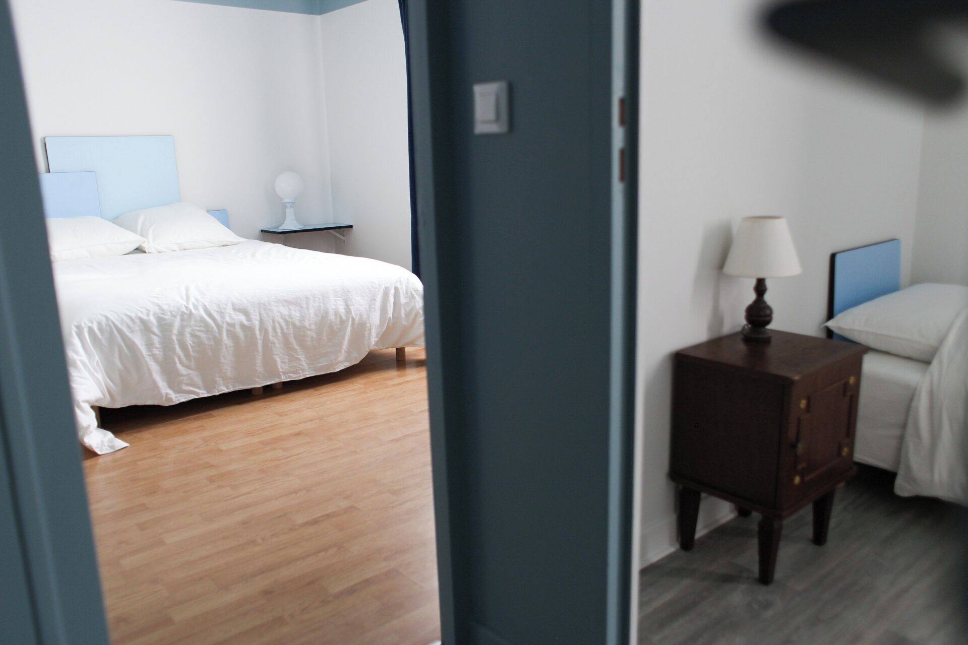 Una habitación de hotel con cama, mesita de noche, lámpara y cabecera azul.