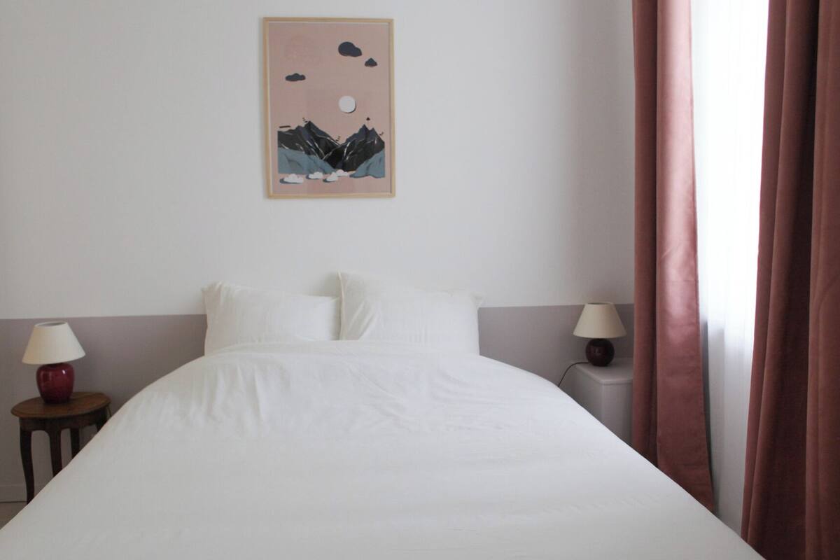 Un lit bien fait dans une chambre d’hôtel, avec une œuvre d’art encadrée au mur et deux lampes de chevet.