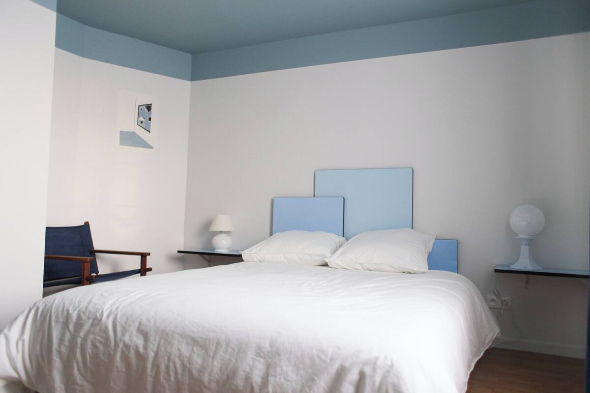Une chambre à coucher comprenant un lit, une chaise, une table de chevet avec une lampe et une étagère fixée au mur, également avec une lampe.