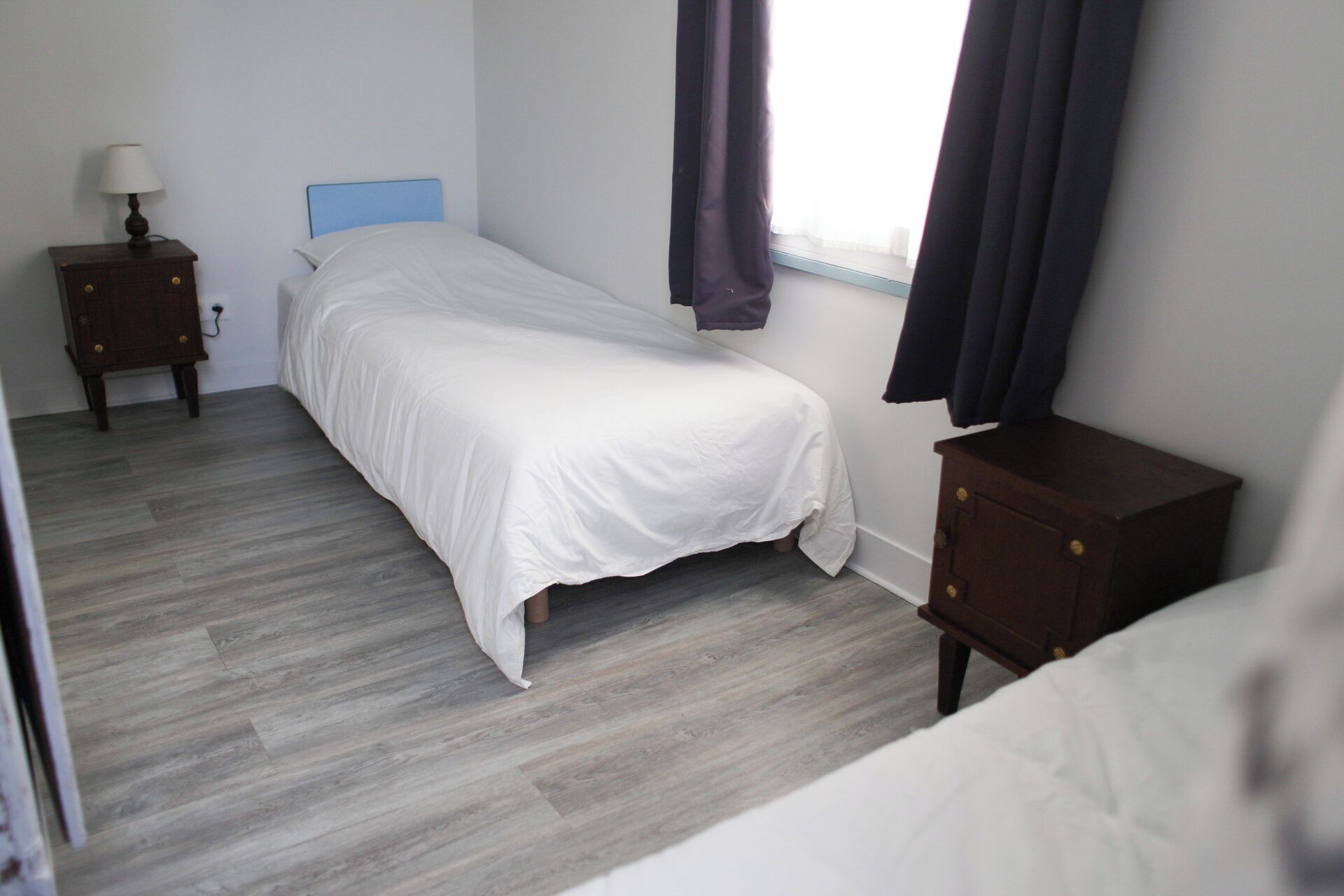 A bedroom with a bed, a nightstand, a dresser, and a window with curtains.