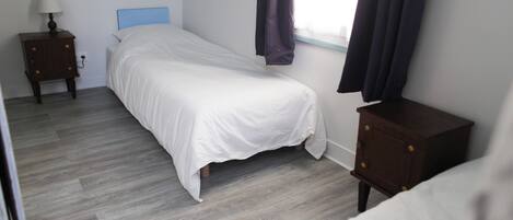 A bedroom with a bed, a nightstand, a dresser, and a window with curtains.