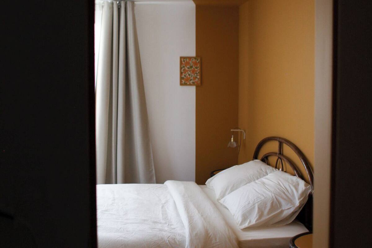 Une petite chambre à coucher peu éclairée, avec un lit simple, une table de chevet et une petite table.