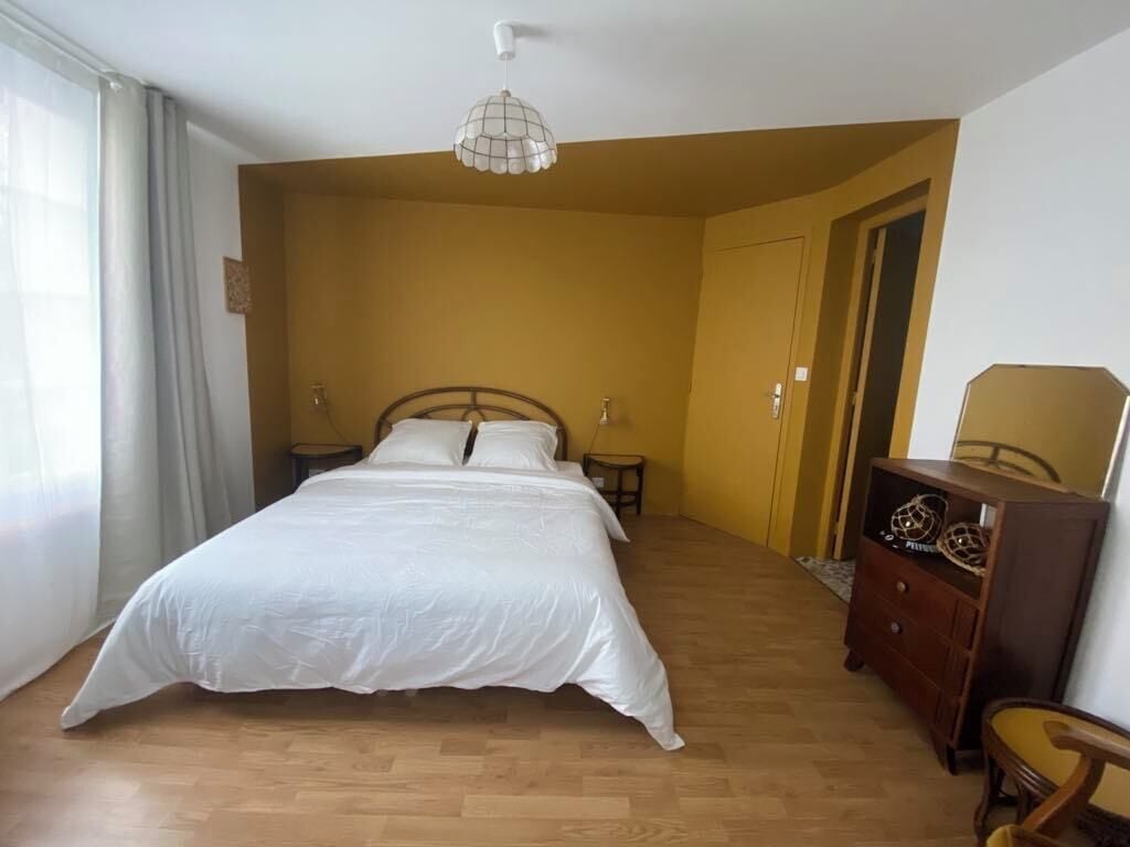 A bedroom with a large bed, wooden flooring, a dresser, and a ceiling light fixture.