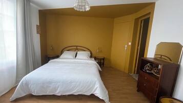 A bedroom with a large bed, wooden flooring, a dresser, and a ceiling light fixture.