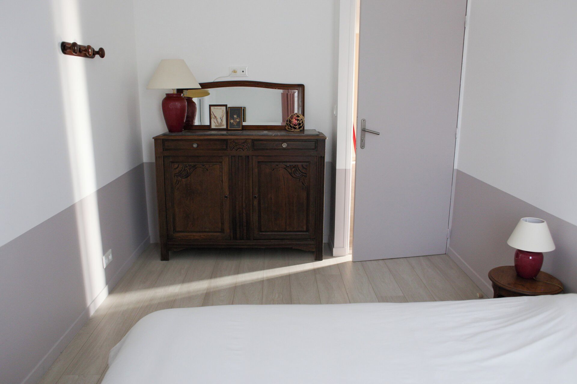 Een slaapkamer met een houten dressoir, een bed en een nachtkastje met een lamp.