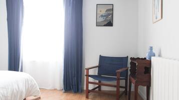 A room with a wooden chair, a bed, a radiator, and a framed picture on the wall.