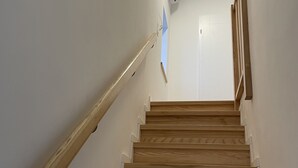 Una escalera de madera con barandilla, paredes blancas y una lámpara en el techo.