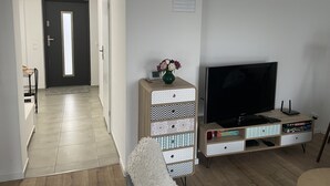 Una sala de estar con televisor, un aparador con cajones decorados y un pasillo que lleva a una puerta.
