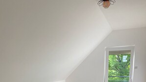 Un dormitorio con una cama de madera, una mesita de noche pequeña, una lámpara y vistas a la vegetación a través de una ventana.