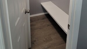 A narrow hallway with a white door on the left, a wooden floor, and a grey wall. There is a white shelf unit with a wooden rod on the right. - Cozy Country Living, just outside the city of Lubbock.  (Shallowater)