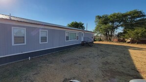 A single-story mobile home with a metal roof, a small porch, and a fenced yard. - Cozy Country Living, just outside the city of Lubbock.  (Shallowater)