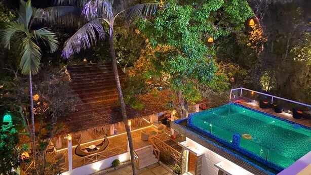 Een nachtzicht van een resort met een zwembad, palmbomen en een gebouw met rieten dak.