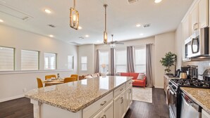 A spacious kitchen with a central island, white cabinetry, a stove, oven, microwave, and a ceiling fan. - Chic 3-Bed Condo, 2-Car Garage close to Pearl & St. Mary's Strip in Tobin Hills! (San Antonio)
