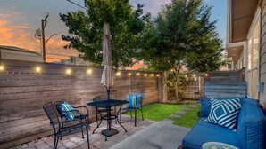 A patio with a blue sofa, two chairs, a small table, and string lights. - Chic 3-Bed Condo, 2-Car Garage close to Pearl & St. Mary's Strip in Tobin Hills! (San Antonio)