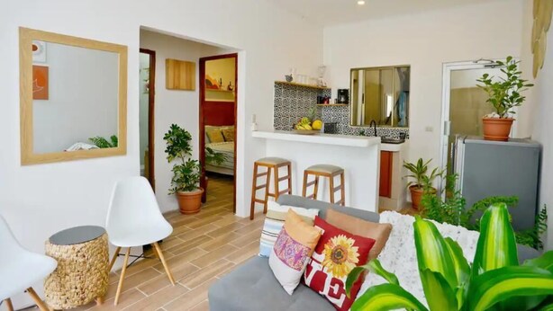 Un espace de vie compact comprenant un coin cuisine, un coin repas et un coin salon avec un canapé et des fauteuils.