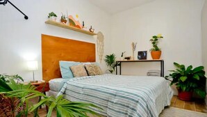 Une chambre à coucher comprenant un lit, une table de chevet, une étagère avec des plantes et une étagère murale ornée d’objets décoratifs.