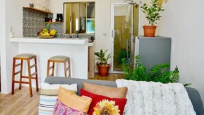 Un espace de vie compact comprenant un coin cuisine, un canapé avec des coussins et une plante en pot.